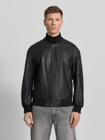 Mannenmodel draagt Regular Fit Lederjacke im College-Stil Modell 'JAKRI' van BOSS Orange in effen zwart, glad leer met ribboorden, ritszakken, metalen label, collegekraag, lang geribde mouwen, regular fit pasvorm, detail in structuur, frontaal volledig lichaam.