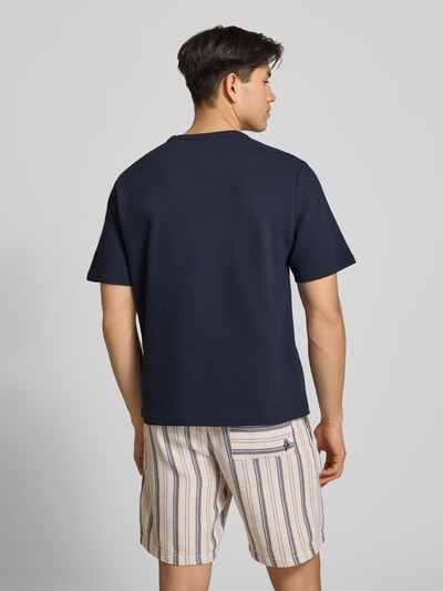 Männermodel trägt T-Shirt mit Label-Stitching von REVIEW, Baumwoll-Mix in Dunkelblau, Waffelstruktur, gerader Schnitt, Ganzkörperansicht Rückansicht.