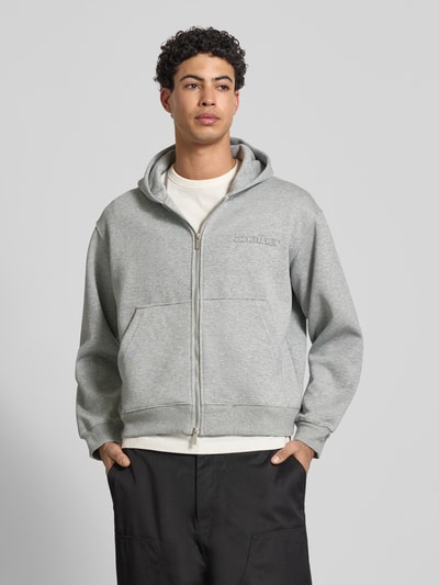 Männermodel trägt Sweatjacke mit Kapuze von ANOTHER COTTON LAB, hellgrauer Baumwoll-Mix, lockerer Schnitt, Front-Reißverschluss, Ganzkörperansicht von vorne.