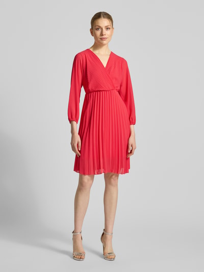 Frauenmodel trägt knielanges Kleid mit Plisseefalten Modell 'Im44sa' von ZABAIONE in Rot, taillierter Schnitt, Wickel-Optik, Ganzkörperansicht von vorne.