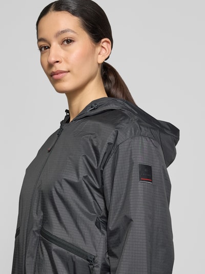 Kobiece model prezentuje czarną kurtkę z kapturem Jacke mit Reißverschlusstaschen Modell 'YADIRA' od FIRE + ICE, krój regular fit, z teksturą w drobną kratkę oraz kieszeniami na zamek, kontekst: długość pleców w rozmiarze 36: 52 cm, szerokość ramion w rozmiarze 36: 45 cm, szerokość w rozmiarze 36: 45 cm, długość rękawa w rozmiarze 36: 61 cm, zbliżenie górnej części ciała z przodu