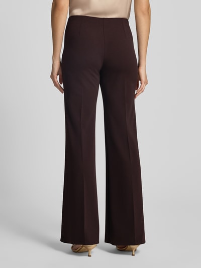 Frauenmodel trägt Flared Fit Stoffhose mit Bügelfalten von Rinascimento in Dunkelbraun, glatte Textur, Ganzkörperansicht Rückansicht. Material-Mic mit Stretch-Anteil, elastischer Bund, Bundweite bei Größe S 38 cm, Innenbeinlänge 85 cm.