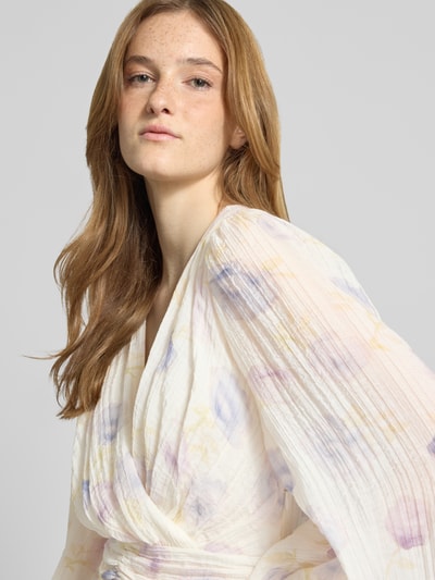 Frauenmodel trägt Minikleid aus Viskose-Mix mit V-Ausschnitt von Gina Tricot, floraler Allover-Print, Langärmelig, Nahaufnahme Oberkörper. Damen Minikleid, taillierte Passform, Raffung, weiche Textur, sanfte Pastelltöne, Kontext: Rückenlänge 84 cm, Brustweite 42 cm, Ärmellänge 70 cm.