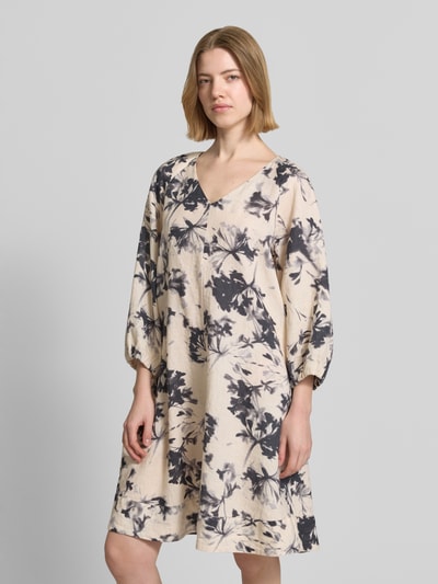 Frauenmodel trägt Fließendes Tunikakleid aus reinem Leinen von Marc O'Polo, Optik:Allover-Muster, Passform fließend, Midi-Länge, V-Ausschnitt, floral, Kurzarm, Ärmelabschluss elastisch, Materialverarbeitung Flammgarn, Material reines Leinen, cremefarben mit dunklem Blumen-Muster, strukturierte Oberfläche, Ganzkörperansicht von vorne.