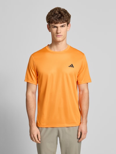 Männermodel trägt T-Shirt mit Logo und Rundhalsausschnitt von adidas Training in Orange, Regular Fit, Logo, Ganzkörperansicht von vorne.
