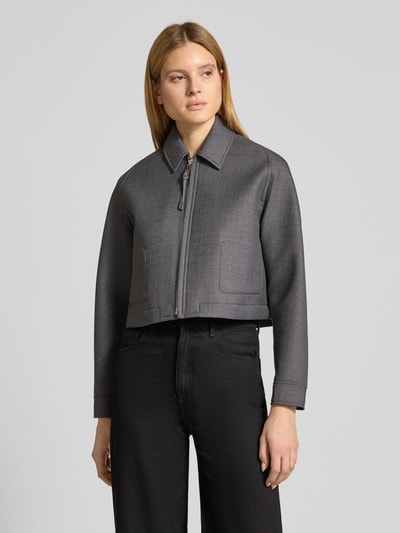 Kobieta modelka nosi kurtkę Relaxed Fit Jacke mit Woll-Anteil Model 'DISCHI' od MAX&Co., efekt: jednolity kolor, długi rękaw, wykładany kołnierz, zamek błyskawiczny, wyhaftowane logo, mankiet, pasek z tyłu, wewnętrzne kieszenie, wykończenie: dżersej; szara, gładka tekstura, prostokątne kieszenie. Ganzkörperansicht z przodu.
