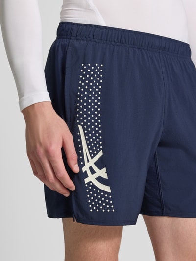 Mężczyznamodel nosi Regular Fit Shorts mit integriertem Slip Modell 'ICON' od ASICS TIGER, nadruk z logo, elastyczny pas, szerokość w rozmiarze M: 37 cm, długość wewnętrzna nogawki w rozmiarze M: 18 cm, ciemnoniebieskie, gładka tekstura, detal boczny, zbliżenie na górną część nogi