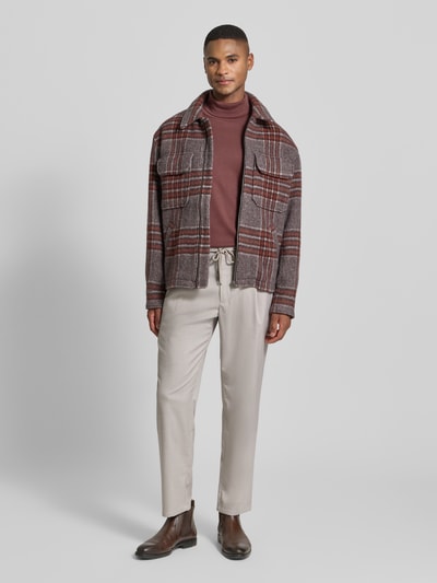 Männermodel trägt Regular Fit Stoffhose mit elastischem Bund von MCNEAL in Beige, kombiniert mit Jacke und Stiefeln, Ganzkörperansicht von vorne. Kontext: Herren Stoffhose von MCNEAL, Regular Fit, Elastischer Bund, Tunnelzug, Französische Eingrifftaschen, Gesäßtaschen, Knopf- und Reißverschluss, Bundweite bei Größe M: 46 cm, Innenbeinlänge bei Größe M: 73 cm.