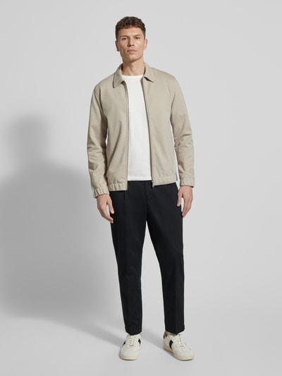 Męski model nosi Regular Fit Chino aus Baumwoll-Mix Modell 'TAAMIR PLEATED' od Armedangels, czarny kolor, krój regular fit, kieszenie boczne i tylne, logo-stitching, bawełniany materiał, mid waist, zdjęcie całej sylwetki z przodu.