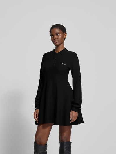 Frauenmodel trägt schwarzes Strickkleid mit Label-Detail von ROTATE, Modal-Woll-Mix, taillierter Schnitt, Hemdblusenkragen, Ganzkörperansicht von vorne.