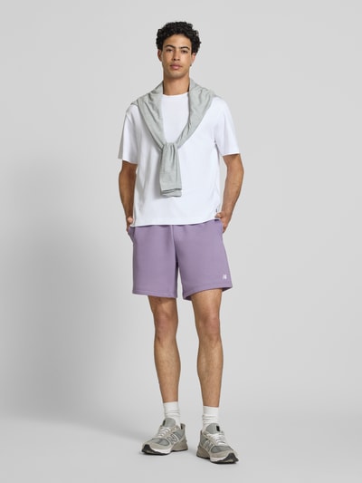 Männermodel trägt Relaxed Fit Shorts mit Logo-Stitching von New Balance in Lila, Baumwoll-Mix, elastischer Bund, Ganzkörperansicht von vorne.