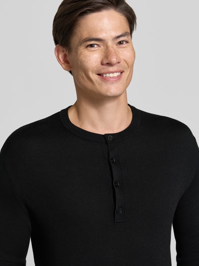 Männermodel trägt schwarzen Strickpullover mit Henley-Kragen von DRYKORN aus reiner Baumwolle, Nahaufnahme Oberkörper.