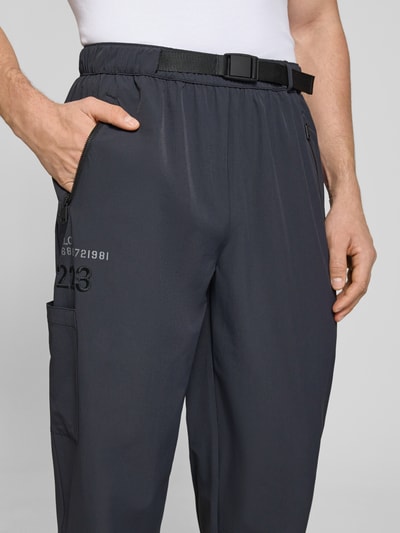 Männermodel trägt Trackpants mit Reißverschlusstaschen Modell 'HALO MOVE' von HALO, Material-Mix mit Stretch-Anteil, Label-Print, Nahaufnahme Oberkörper.