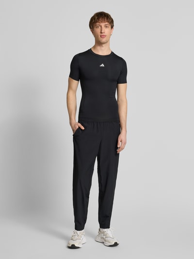 Männermodel trägt schwarzes T-Shirt mit Label-Print von adidas Training, Slim Fit, Material-Mix, gerippter Rundhalsausschnitt, Ganzkörperansicht von vorne.