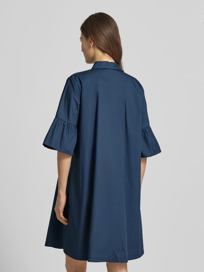 Frauenmodel trägt knielanges Hemdblusenkleid mit Kentkragen Modell 'EPOCHE' von EMME aus reiner Baumwolle, lockerer Schnitt, Volants, Farbe Dunkelblau, Rückenlänge 93 cm bei Größe 36, Ganzkörperansicht Rückansicht.