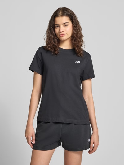 Frauenmodel trägt Regular Fit T-Shirt mit Logo-Stitching von New Balance, Damen T-Shirt aus Reine Baumwolle, Rundhalsausschnitt, Rückenlänge 60 cm, schwarze Farbe, glatte Struktur, Ganzkörperansicht von vorne.
