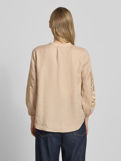 Frauenmodel trägt Leinenbluse mit Motiv-Stitching und Quasten-Details von Emily Van den Bergh in Beige, elastische Ärmelabschlüsse, Loose-Fit, reine Leinenqualität, Rückenlänge 64 cm, Ärmellänge 50 cm, Ganzkörperansicht Rückansicht.