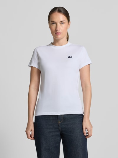 Vrouwenmodel draagt Slim Fit Sport-T-Shirt aus Baumwoll-Mix van Lacoste voor dames in wit met donkerblauw logo, Ganzkörperaanzicht van voren
