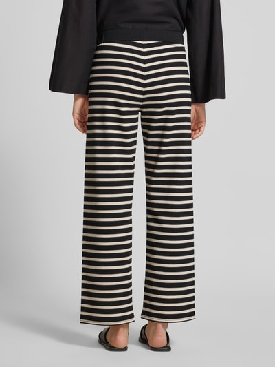 Frauenmodel trägt Hose im Allover-Look Modell 'Filiz' von STEHMANN aus Baumwoll-Mix mit Stretch-Anteil, Relaxed-Fit, elastischer Bund, Querstreifen in Schwarz und Beige, strukturierte Oberfläche, Ganzkörperansicht Rückansicht.