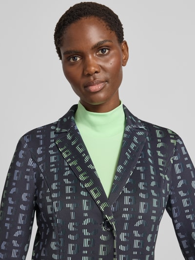 Frauenmodel trägt Slim Fit Blazer mit Logo-Detail von Marc Cain in Dunkelblau mit grünem Muster und Reverskragen, Nahaufnahme Oberkörper, elastischer Material-Mix, aufgesetzte Taschen, 2-Knopfleiste.