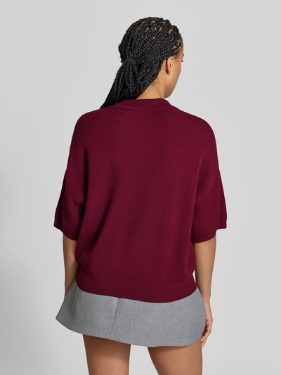 Frauenmodel trägt Cropped Boxy Fit Strick-Poloshirt von ROTATE in Dunkelrot mit gerippten Abschlüssen, Material-Mix, Rückenansicht, Ganzkörperansicht Rückansicht.