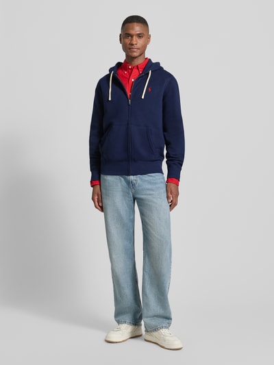 Męski model nosi Sweatjacke mit Kapuze od Polo Ralph Lauren, bawełniana mieszanka, luźny krój, ciemnoniebieski kolor, widok całej sylwetki z przodu.