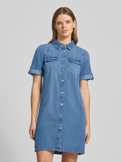 Kobiece modelka nosi produkt Körpernahes Jeanskleid aus Baumwoll-Viskose-Mix Modell 'LISA' od Only, mini długość, V-dekolt, krótkie rękawy, jednolity niebieski denim, kieszenie na piersi, faktura gładka, widoczne przeszycia, widok z przodu całej sylwetki.