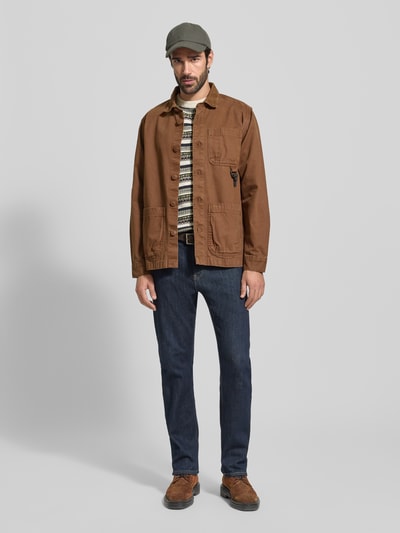 Männermodel trägt Loose Fit Strickpullover aus reiner Baumwolle von Barbour mit all-over Noors motief, labelpatch, bruine tinten, gebreide textuur, lange mouwen, ronde hals, rompzoom en mouwboorden, geheel beeld van voren.
