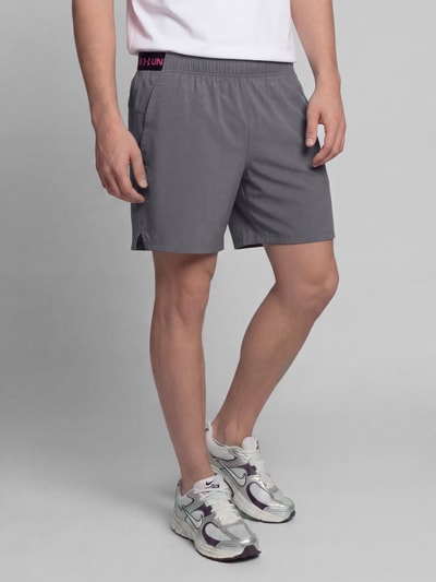 Männermodel trägt graue Regular Fit Sportshorts mit Logo-Print von Under Armour, glatte Textur, Ganzkörperansicht von vorne, Herren Sportshorts von Under Armour.