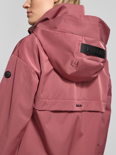 Frauenmodel trägt Jacke mit Stehkragen von khujo in Altrosa, glatte Textur, Kapuze, Markenaufdruck, Detailaufnahme Rückenansicht. Rückenlänge 60 cm, Schulterbreite 51 cm, Brustweite 50 cm, Ärmellänge 54 cm bei Größe S.