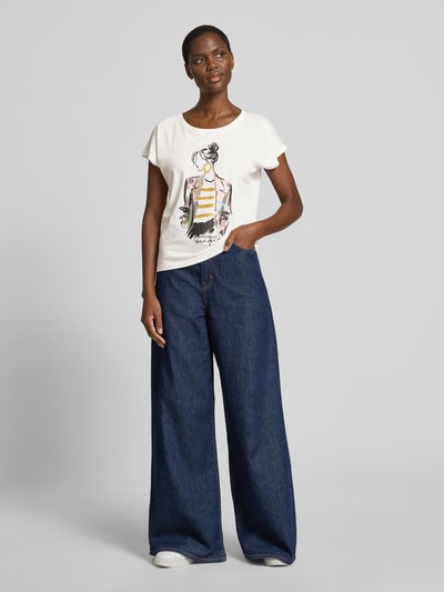 Frauenmodel trägt Damen T-Shirt mit Motiv- und Statement-Print von Christian Berg Woman aus Baumwoll-Viskose-Mix, Regular-Fit, weiß, Rundhalsausschnitt, dunkle weite Jeans, Rückenlänge bei Größe S 57 cm, Ganzkörperansicht von vorne.