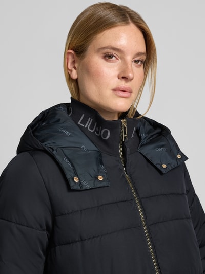 Frauenmodel trägt Regular Fit Mantel mit Logo-Detail von Liu Jo Sport in Stepp-Optik, dunkle Farbe, Kapuze, Reißverschluss, Nahaufnahme Oberkörper