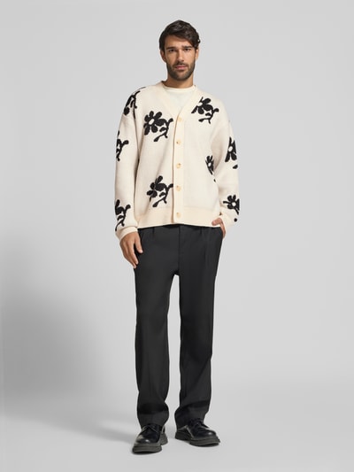 Männermodel trägt Strickjacke im Allover-Look Modell 'DIA INTARCIA' von Casual Friday in Creme mit schwarzen Blumenmustern, Relaxed Fit, Woll-Mix, Knopfleiste, V-Ausschnitt, schwarze Stoffhose und schwarze Schuhe, Ganzkörperansicht von vorne.