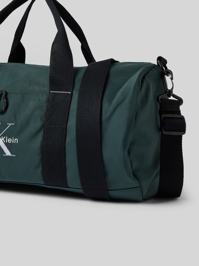 Produktfoto, Weekender met labelstitching van CK Calvin Klein in donkergroen met zwarte draagband, afneembare schouderband, rits op het hoofdvak, binnenvak met ritssluiting, maat 1 breedte 45 cm, lengte 24 cm, diepte 22 cm, schouderbandlengte 90 cm.