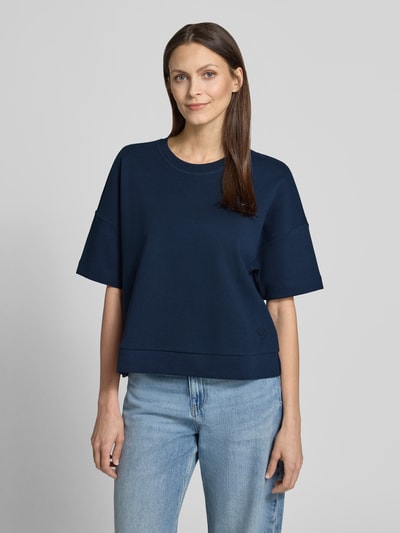 Frauenmodel trägt Boxy Fit T-Shirt Modell 'Tilina' von JOOP! im Baumwoll-Mix mit Rundhalsausschnitt in Dunkelblau, Nahaufnahme Oberkörper.