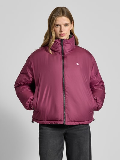 Modelka kobieca nosi Jacke mit Logo-Print od Calvin Klein Jeans w kolorze amarantowym, prosty krój, unikatowy design, stójka, logo na piersi, elastyczne mankiety, długość tyłu w rozmiarze M: 66 cm, szerokość ramion w rozmiarze M: 63 cm, szerokość klatki piersiowej w rozmiarze M: 60 cm, długość rękawa w rozmiarze M: 63 cm, tekstura gładka, widok całej sylwetki z przodu.