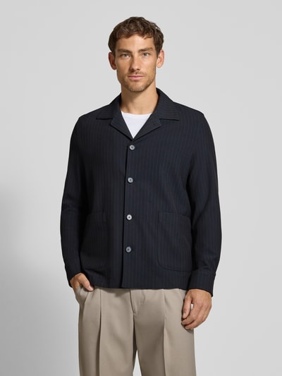 Männermodel trägt dunkelblaues Oversized Fit Freizeithemd mit Viskose-Anteil Modell 'Malte' von CINQUE, dezentes Streifenmuster, Kombi mit beigen Hosen, Nahaufnahme Oberkörper, elastischer Material-Mix, Reverskragen, langärmeliges Design, Rückenlänge bei Größe M: 75 cm.