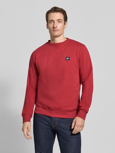 Männermodel trägt Regular Fit Sweatshirt aus Baumwoll-Mix von LERROS, rote Farbe, Logo-Patch, Jeans kombiniert, Ganzkörperansicht von vorne.