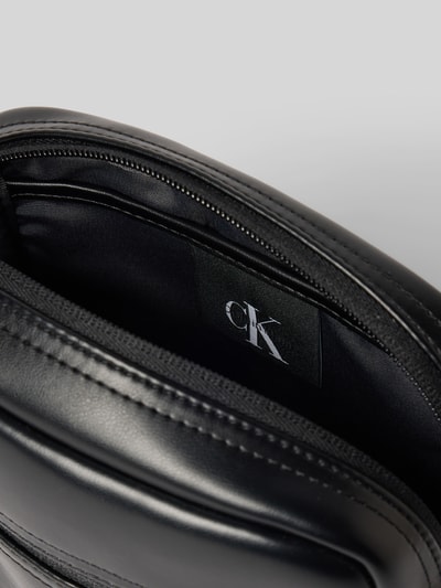 Produktfoto, schwarze Herren Umhängetasche mit glatter Textur, Logo-Prägung und Label von CK Calvin Klein, Nahaufnahme Innenansicht