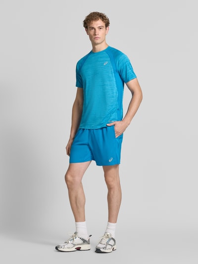 Męski model nosi Regular Fit Shorts mit integriertem Slip Modell 'Core' od ASICS TIGER w kolorze niebieskim, nadruk z logo, elastyczny pas, szerokość w rozmiarze M: 38 cm, długość wewnętrzna nogawki w rozmiarze M: 17 cm, widok całej sylwetki z przodu.