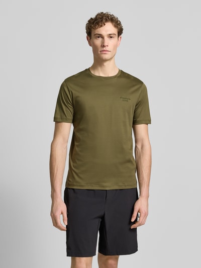 Męski model nosi Regular Fit T-Shirt aus reiner Baumwolle Modell 'PS Spirit 70 Grx' von BOSS Green X PORSCHE, oliwkowy, krótki rękaw, okrągły dekolt, jednolity, aplikacja z logo, materiał 4way stretch, bawełna, całkowity widok z przodu.