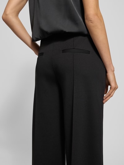 Frauenmodel trägt Wide Leg Stoffhose mit fixierten Bügelfalten Modell 'KATE' von ICHI, dunkles Material-Mix mit Viskose-Anteil, Paspeltaschen am Gesäß, Ganzkörperansicht Rückansicht.