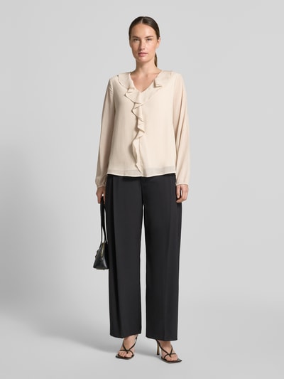 Frauenmodel trägt Regular Fit Langarmbluse in Crêpe-Optik von s.Oliver BLACK LABEL in Beige mit Rüschen, kombiniert mit schwarzer Hose, Ganzkörperansicht von vorne.
