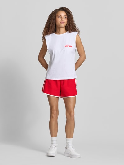 Frauenmodel trägt Track Shorts mit elastischem Bund und Label-Detail von Karo Kauer in Rot, Material-Mix mit Stretch-Anteil, Loose-Fit, Ganzkörperansicht von vorne
