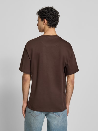 Männermodel trägt Regular Fit T-Shirt mit Logo-Stitching von KARL KANI in Braun, Kurzärmelig, Rundhalsausschnitt, Rückenlänge 74 cm, Ganzkörperansicht Rückansicht.