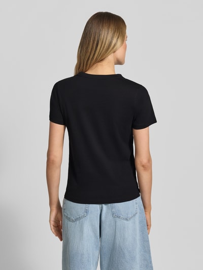 Frauenmodel trägt T-Shirt mit Label-Print und Strasssteinbesatz von Guess aus Reine Baumwolle, Straight Fit, Rundhalsausschnitt, Rückenlänge 59 cm, Ganzkörperansicht Rückansicht.