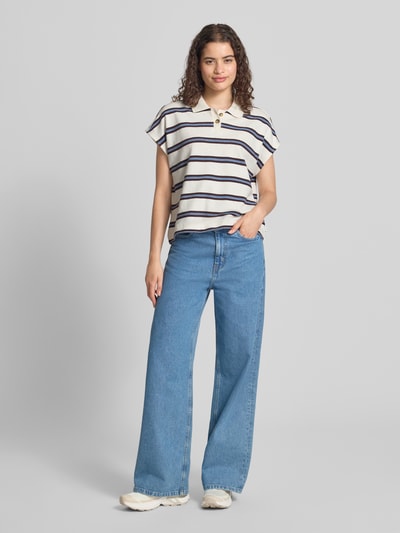 Frauenmodel trägt Regular Fit Poloshirt aus reiner Baumwolle von Marc O'Polo DENIM in Creme mit Streifen, kombiniert mit blauer Jeans, Ganzkörperansicht von vorne.