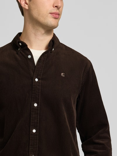 Männermodel trägt Regular Fit Freizeithemd mit Logo-Stitching Modell 'MADISON' von Carhartt Work In Progress aus brauner Baumwolle, Nahaufnahme Oberkörper.