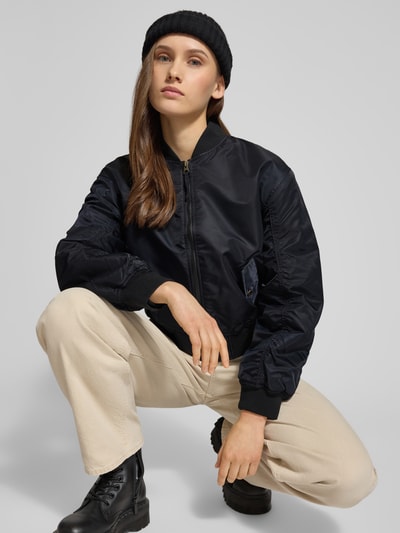 Frauenmodel trägt Bomberjacke mit Stehkragen und Reißverschluss Modell 'SCOUT' von Levi's®, schwarze Farbe, glatte Textur, Ganzkörperansicht von vorne. Regular Fit, Pattentaschen, Rückenlänge 50 cm, Schulterbreite 42 cm, Brustweite 40 cm, Ärmellänge 59 cm.