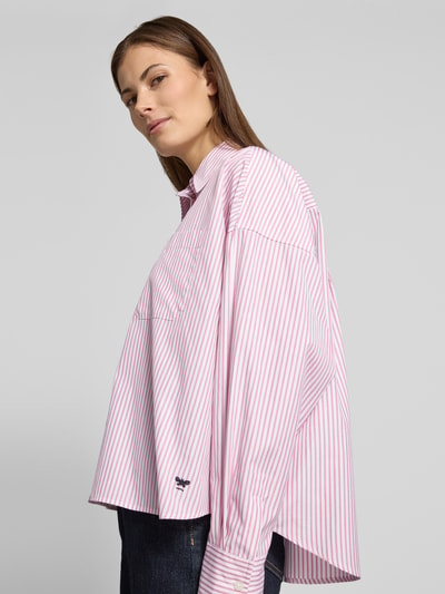 Modelka nosi Oversized Hemdbluse aus reiner Baumwolle Modell 'AUREO' od Weekend Max Mara, różowe i białe paski, logo, bawełna, widok z przodu.